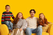© Pixel-Shot - Happy family in warm sweaters sitting on sofa near yellow wall
