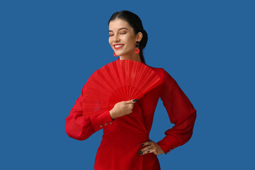 Wall Mural - Beautiful young happy woman with fan on blue background. Chinese New Year celebration