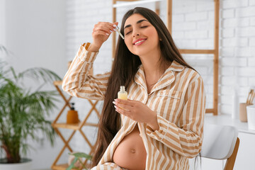 Wall Mural - Beautiful pregnant woman applying cosmetic product on face at home