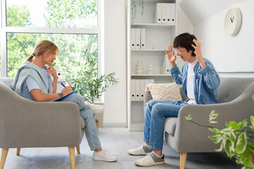 Wall Mural - Angry teenage boy sitting on sofa at psychologist's office