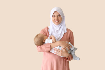 Canvas Print - Happy Muslim mother in hijab with cute little baby on beige background