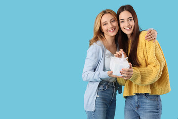 Wall Mural - Pretty young woman with her mother and gift box on blue background