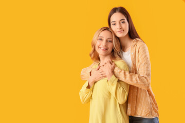 Wall Mural - Pretty young woman hugging her mother on yellow background. International Hug Day