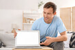 © Pixel-Shot - Young man with blank laptop sitting on sofa at home
