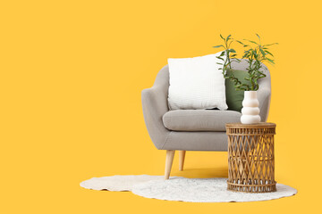 Canvas Print - Table with bamboo stems in vase, grey armchair and rug on yellow background