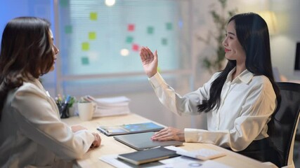 Wall Mural - Two women are talking in a room with a laptop on the table. Scene is professional and serious