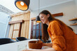© SHOTPRIME STUDIO - Smiling woman preparing healthy food in a modern kitchen, wearing an orange shirt, showcasing a joyful cooking experience with natural light