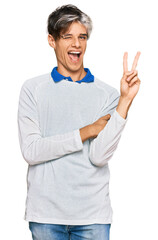 Wall Mural - Young hispanic man wearing casual clothes smiling with happy face winking at the camera doing victory sign. number two.