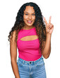 © Krakenimages.com - Young hispanic woman with curly hair wearing pink top smiling with happy face winking at the camera doing victory sign. number two.