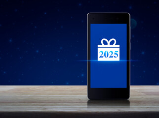 Wall Mural - Gift box happy new year 2025 icon on modern smart mobile phone screen on wooden table over fantasy night sky and moon, Business happy new year 2025 shop online concept