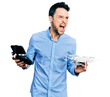 © Krakenimages.com - Hispanic man with beard using drone with remote control angry and mad screaming frustrated and furious, shouting with anger. rage and aggressive concept.
