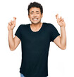 © Krakenimages.com - Young handsome man wearing casual black t shirt gesturing finger crossed smiling with hope and eyes closed. luck and superstitious concept.