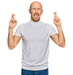 © Krakenimages.com - Bald man with beard wearing casual white t shirt gesturing finger crossed smiling with hope and eyes closed. luck and superstitious concept.