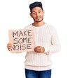 © Krakenimages.com - Handsome latin american young man holding make some noise banner looking positive and happy standing and smiling with a confident smile showing teeth