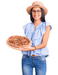 © Krakenimages.com - Young beautiful latin girl wearing summer hat and glasses holding pizza looking positive and happy standing and smiling with a confident smile showing teeth