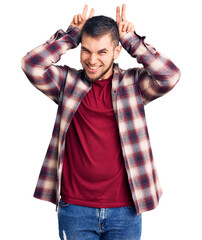 Wall Mural - Young handsome man wearing casual shirt posing funny and crazy with fingers on head as bunny ears, smiling cheerful