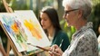 © mashimara - Senior woman painting a scenic landscape outdoors on an easel, embracing creativity and inspiration amidst nature.