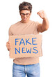 © Krakenimages.com - Young handsome man holding fake news banner annoyed and frustrated shouting with anger, yelling crazy with anger and hand raised