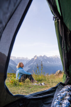 Young woman relaxing by the tent in Alps mountains overlooking Mont Blanc peak. Sustainable tourism in Chamonix, France