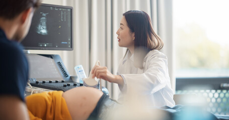 Aufkleber - Expectant Couple Attending Prenatal Ultrasound Appointment. Asian Doctor Conducts Scan, Explaining Fetal Development Using Monitor Display. Pregnant Woman Smiles, Partner Observes Supportively