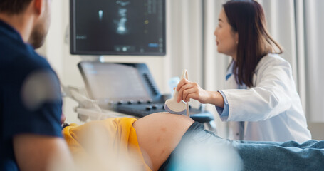 Aufkleber - Caring Female Hospital Obstetrician Conducting an Ultrasound Exam for a Pregnant Woman. Young Couple Watching the Screen while Asian Doctor Describes the Baby’s Growth to Expectant Mother