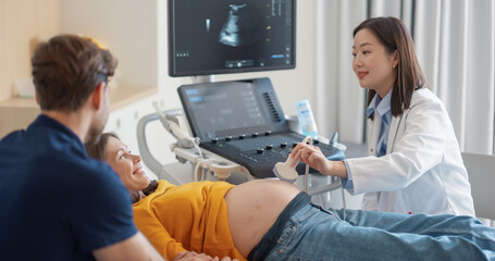 Aufkleber - Expectant Couple Attending Prenatal Ultrasound Appointment. Asian Doctor Conducts Scan, Explaining Fetal Development Using Monitor Display. Pregnant Woman Smiles, Partner Observes Supportively