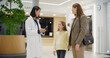 © Gorodenkoff - Asian Female Doctor Greets a Young Mother with a Daughter in Modern Hospital Lobby, Talking to Them before Going to the Medical Office. Visitors Interacting with a Healthcare Professional