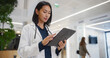 © Gorodenkoff - Portrait of an Asian Female General Practitioner Using Tablet Computer to as She is Browsing Insights About a Complex Medical Case. Healthcare Workers Walking Through a Modern Hospital Hall