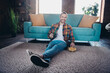 © deagreez - Young man enjoying a relaxing day at home sitting on carpet with chips and drink