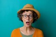 © Rohit k  - Elderly woman with curly hair, in a stylish hat and orange sweater, showing genuine surprise on a vibrant teal background, capturing a striking portrait