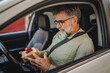 © Miljan Živković - Senior mature man sit in the car and hold small gift with red ribbon