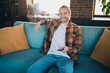 © deagreez - Joyful young man with casual style relaxing on a cozy sofa in bright living room holding remote control enjoying leisure