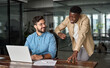 © insta_photos - Happy Latin team leader teaching young male African coworker explaining online project strategy. Two busy diverse professional software engineers working in teamwork talking at work desk with laptop.