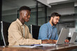 © insta_photos - Two busy diverse business men company employees using laptops working in office. Professional young businessmen colleagues workers typing on computer technology at office workplace desk.