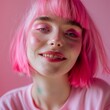 © Elena L - A person with vibrant pink hair and makeup smiles warmly against a soft pink background, exuding playful charm and bright expressiveness.