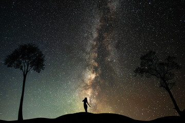 Wall Mural - Silhouette of a woman and trees on the against starry sky with Milky Way galaxy. 