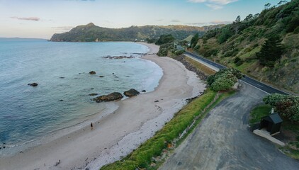 Wall Mural - Coastal scene; person walks along beach; scenic road winds along the shore. K?AOTUNU, WHITIANGA, COROMANDEL PENINSULA, NEW ZEALAND