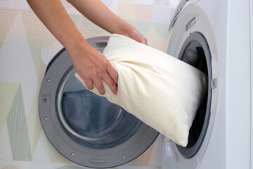 Man's hand holds a pillow and puts it in the washing machine.