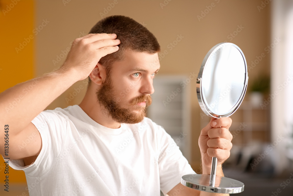 Handsome young man with hair loss problem and mirror at home
