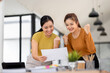 © David - Two asian young women use laptop to work at workplace and lift her arm showing happiness teamwork celebrating achievement and success concept.