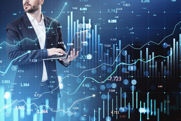 Wall Mural - Businessman analyzing financial data on laptop with stock market graphs and charts in background.