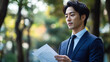 © Suriyo - Businessman in Suit Reading Documents Outdoors in Beautiful Nature Background with Soft Focus