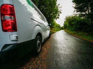 Wall Mural - A white medium size van is parked on a small county road in rural area with a red tail light. The road is empty and the sun is shining brightly. Product delivery to remote locations concept.
