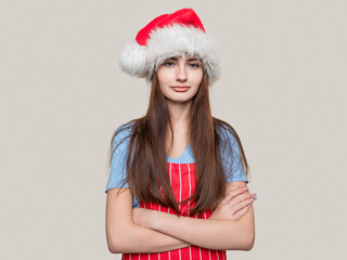 Wall Mural - Young teenager girl wearing blue shirt, Santa Claus hat and red and white apron on light color background. Cooking for special event concept. Model with long high volume hair and slim body type.