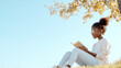 © Ari - Afro girl sitting on grass under the tree reading a book studying
