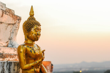 Golden Buddha statue is positioned in a seated posture with gold leaf on surface at sunset