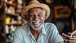 © marimalina - Smiling elderly man wearing straw hat seated inside a cozy workshop filled with handmade crafts, enjoying the warmth of community in the afternoon sunlight