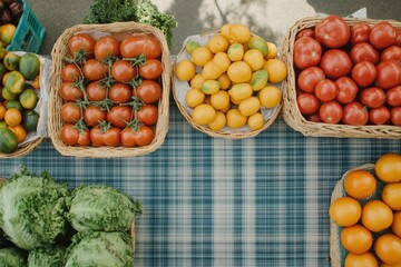 Aufkleber - Colorful baskets filled with fresh tomatoes, lemons, and greens are arranged on a checkered tablecloth at a bustling farmers market. Generative AI