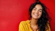 © Vikarest - A beautiful young woman with wavy dark hair in a yellow blouse on a red background smiles and looks to the side.