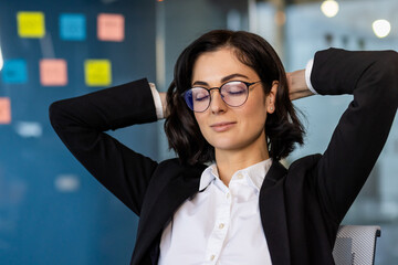 Poster - Businesswoman relaxing at office desk, eyes closed, hands behind head. Displays calmness, work life balance, stress relief in modern workplace setting. Corporate professional enjoying break from work